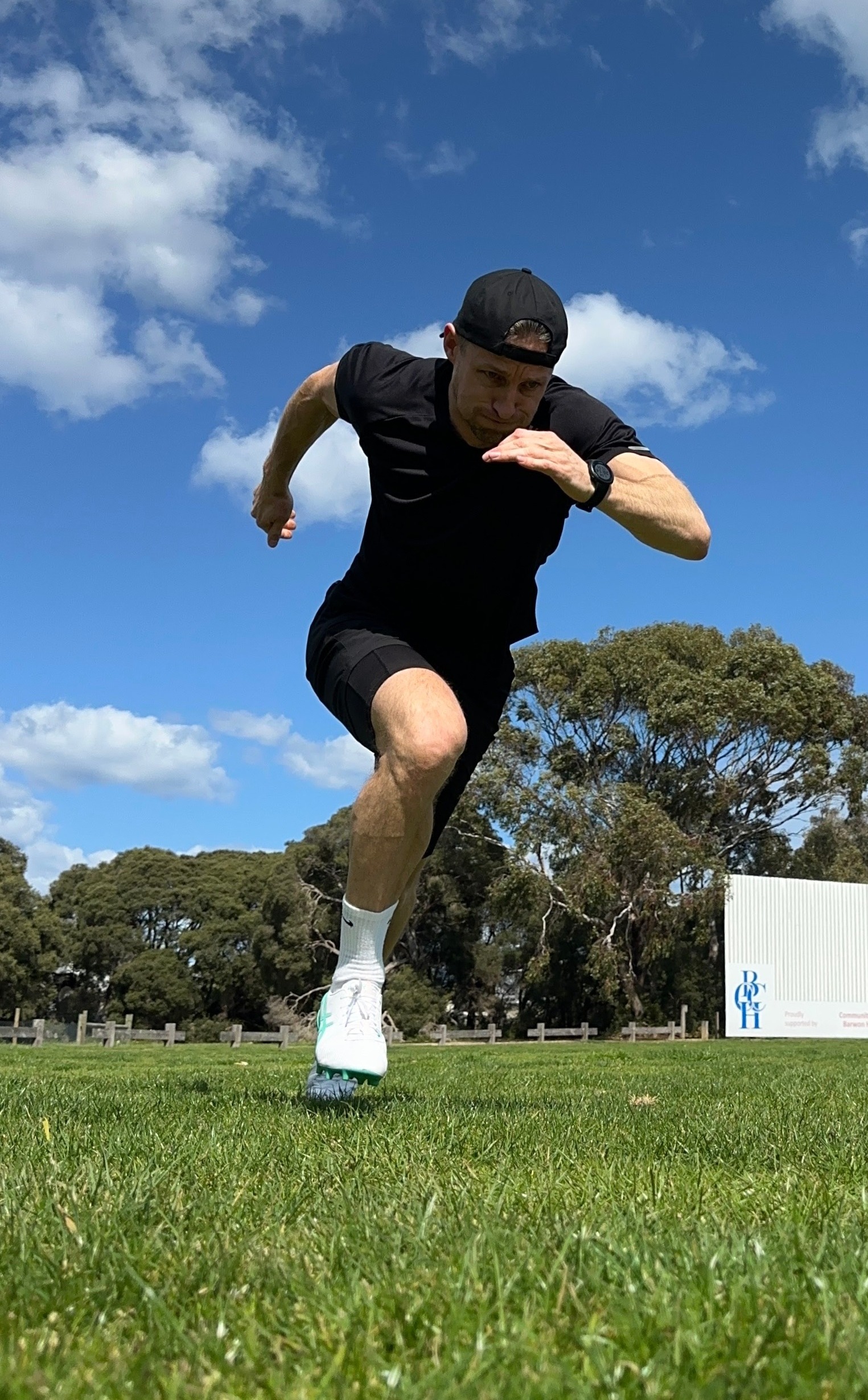Footballer player sprinting across a grass training field under a blue sky